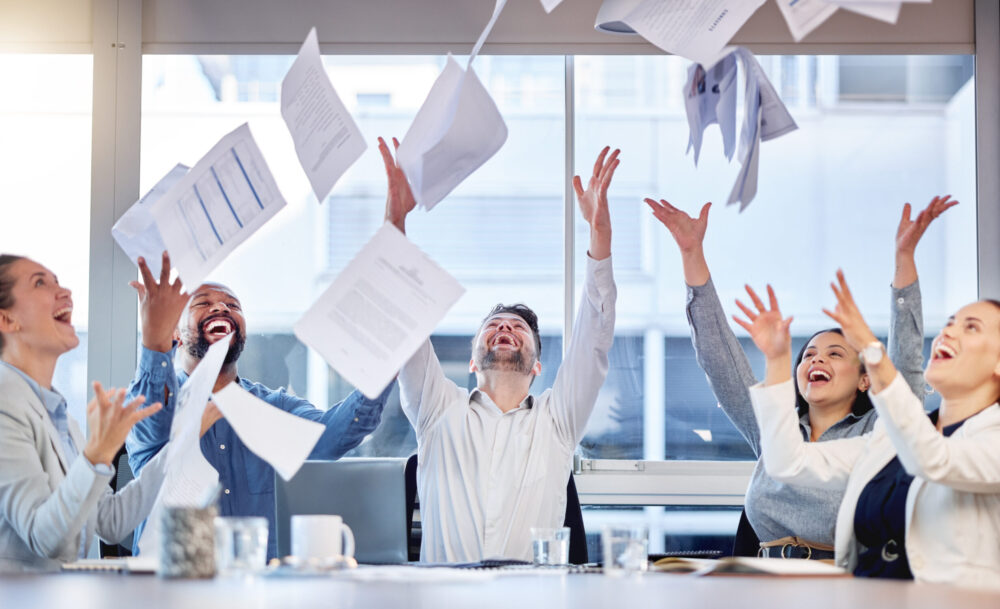 Group celebrating with papers flying in office
